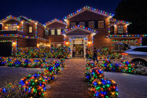 Two-story brick home decorated with professional multi-color Christmas lights along the roofline and landscaping at night