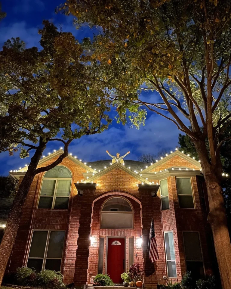 Brick home with warm white Christmas lights under oak trees