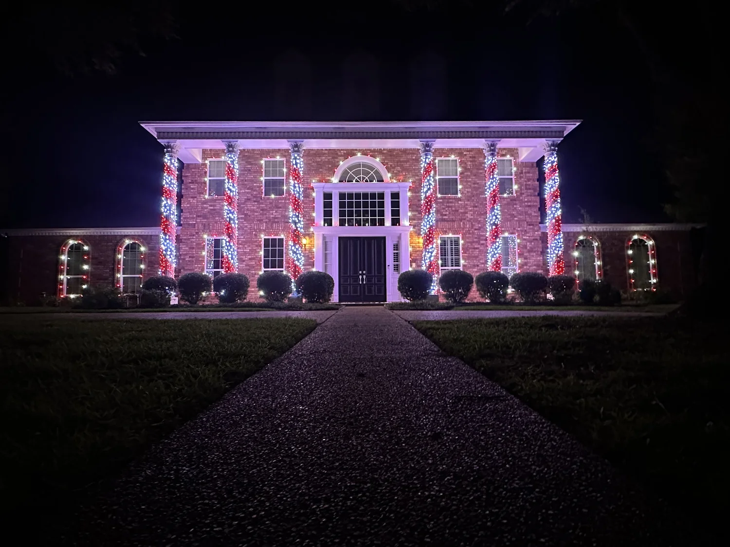 Brick home with red and white Christmas lights wrapped on its pillars, a Grants Outdoor install
