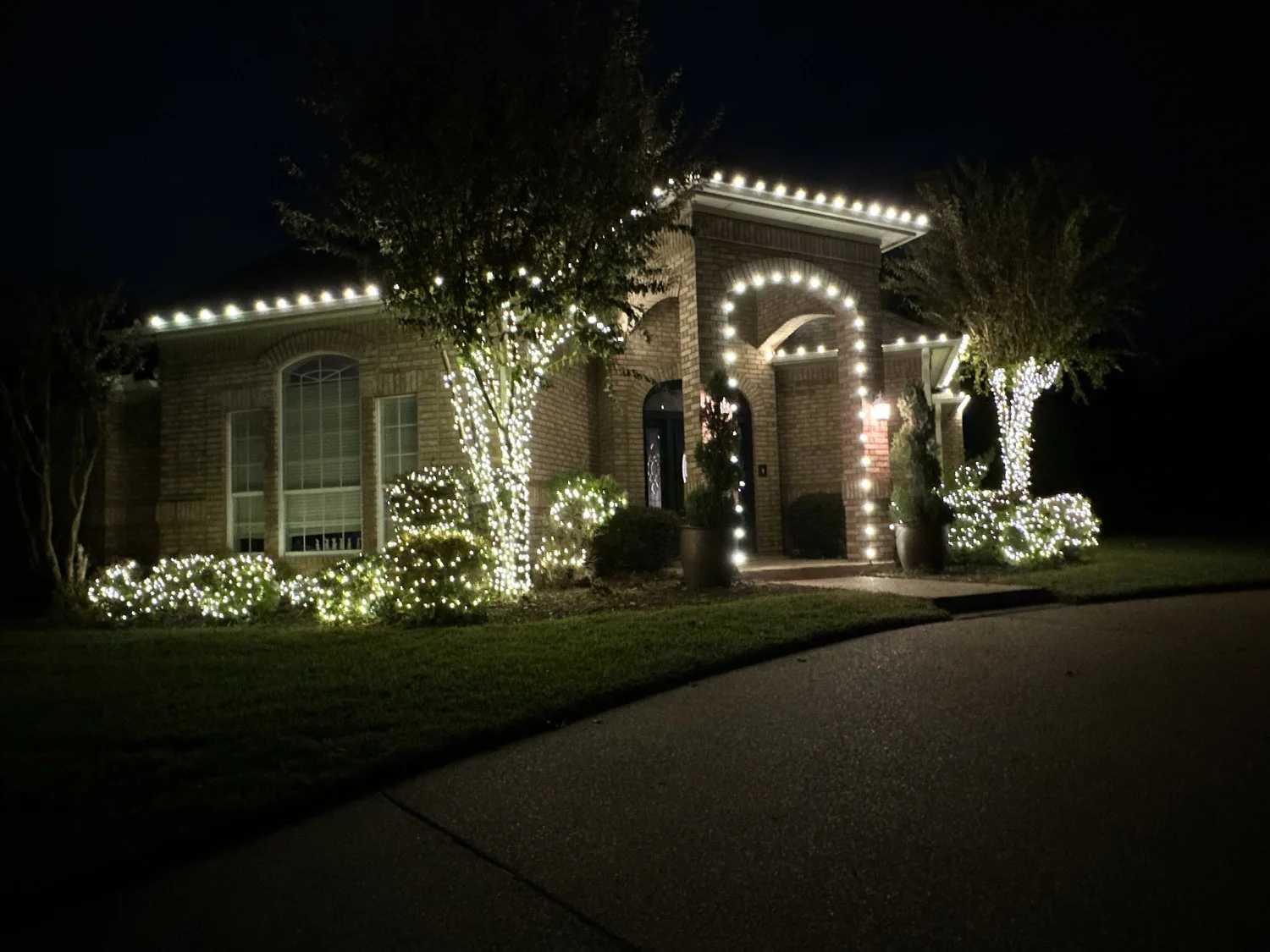 Home with warm white roofline Christmas lights and wrapped trees